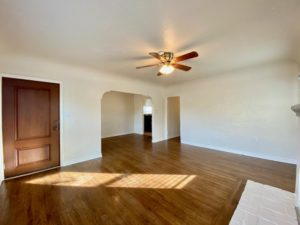 vacant living room with wood floors- ceiling fan and wood door