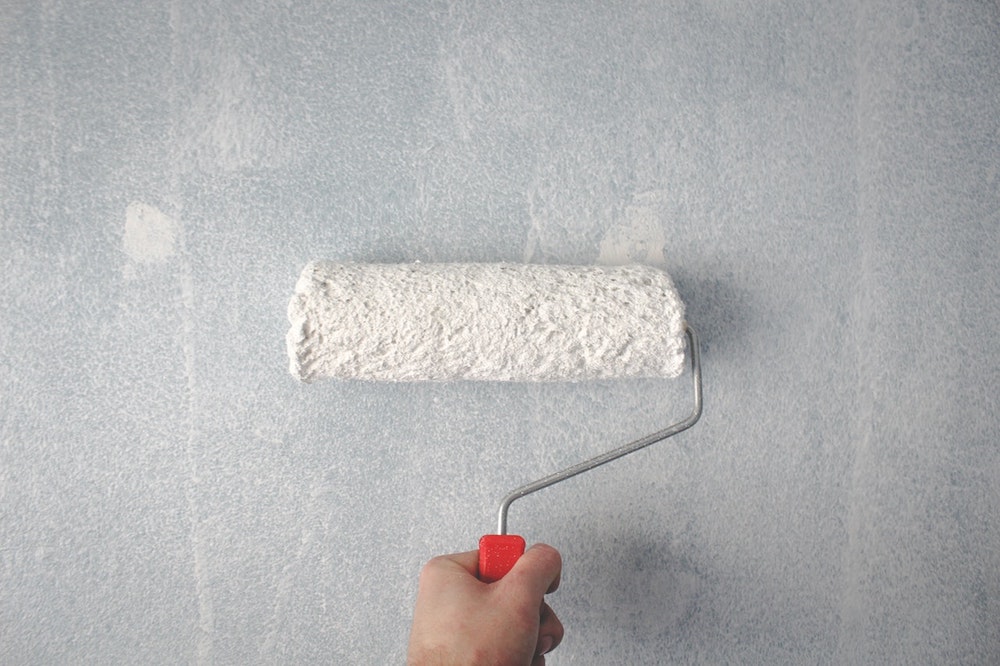 Person holding a paint roller on a wall.