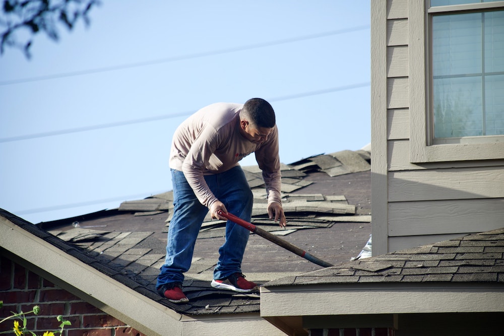 A man fixing up a roof of a home while standing on top of it.