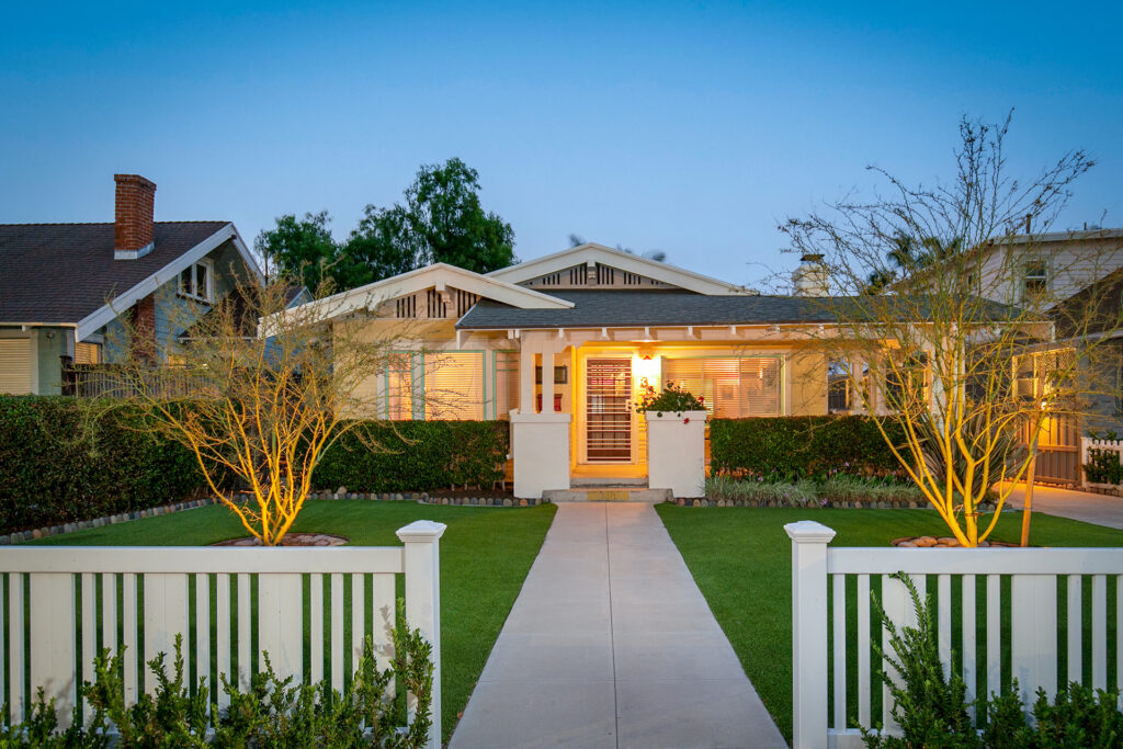 Lush front yard and craftsman-style home at dusk in North Park, San Diego, featuring professional landscape lighting and a white picket fence