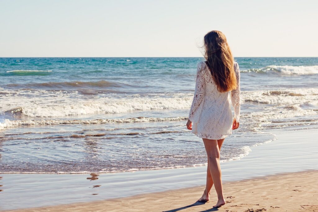 Woman standing on the shore of the beach staring into the water