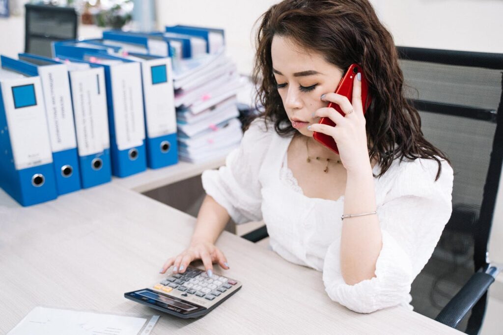 A Woman Using a Calculator while Talking on the Phone