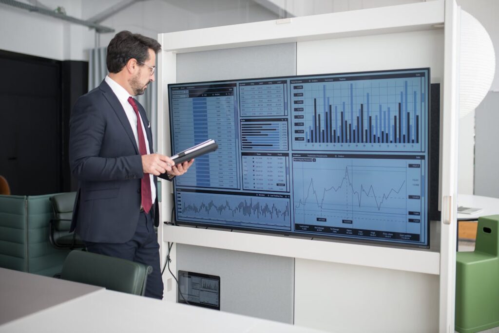 Man in Corporate Attire Looking at a Wide Screen Monitor with Fluctuating Bars and Graphs