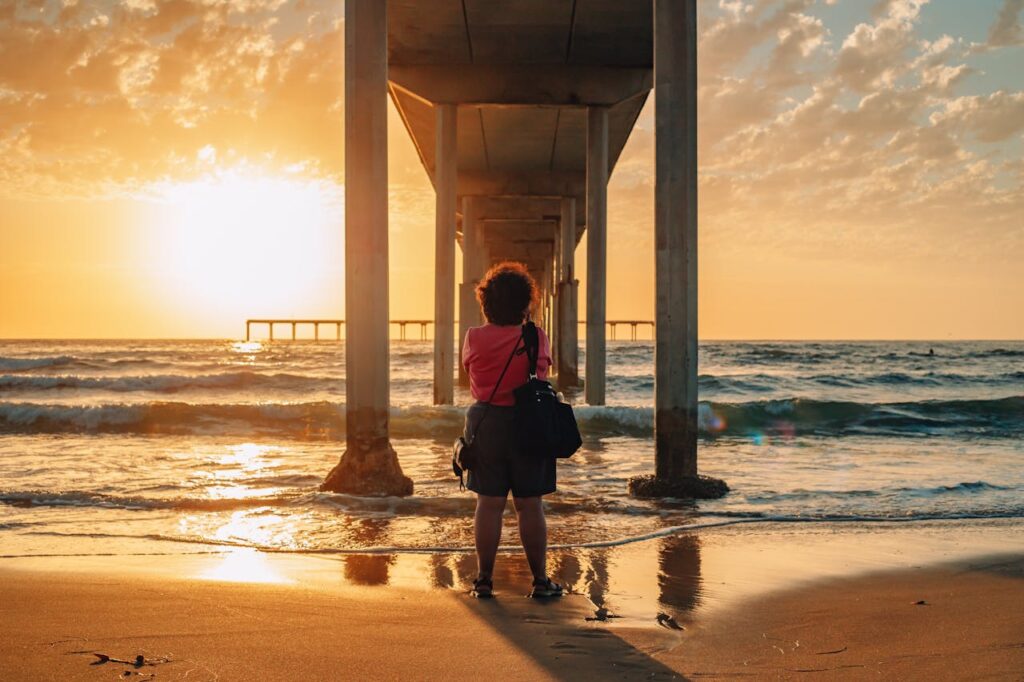 A Woman in a Pink Shirt under a Pier at a Shore
