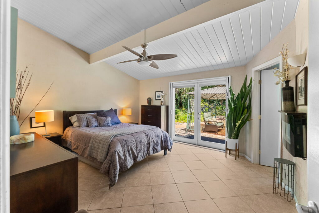 large bedroom with grey bedding, brown furniture and open french doors to outside