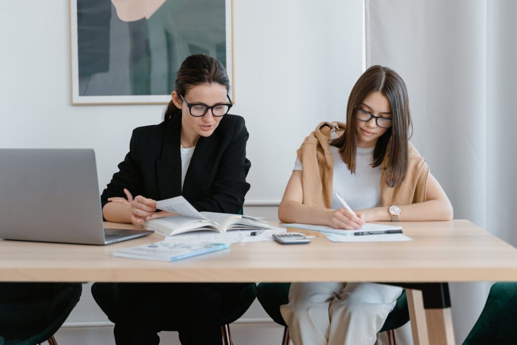 Two Women in a Wooden Table Reading and Using a Calculator