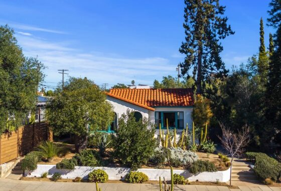 Spanish-style home at A view of the backyard garden with a brick pathway, a large agave plant, and the white stucco house with a second-story deck at 3237-39 Dale St featuring a red tile roof, white stucco exterior, and mature drought-tolerant landscaping in North Park.